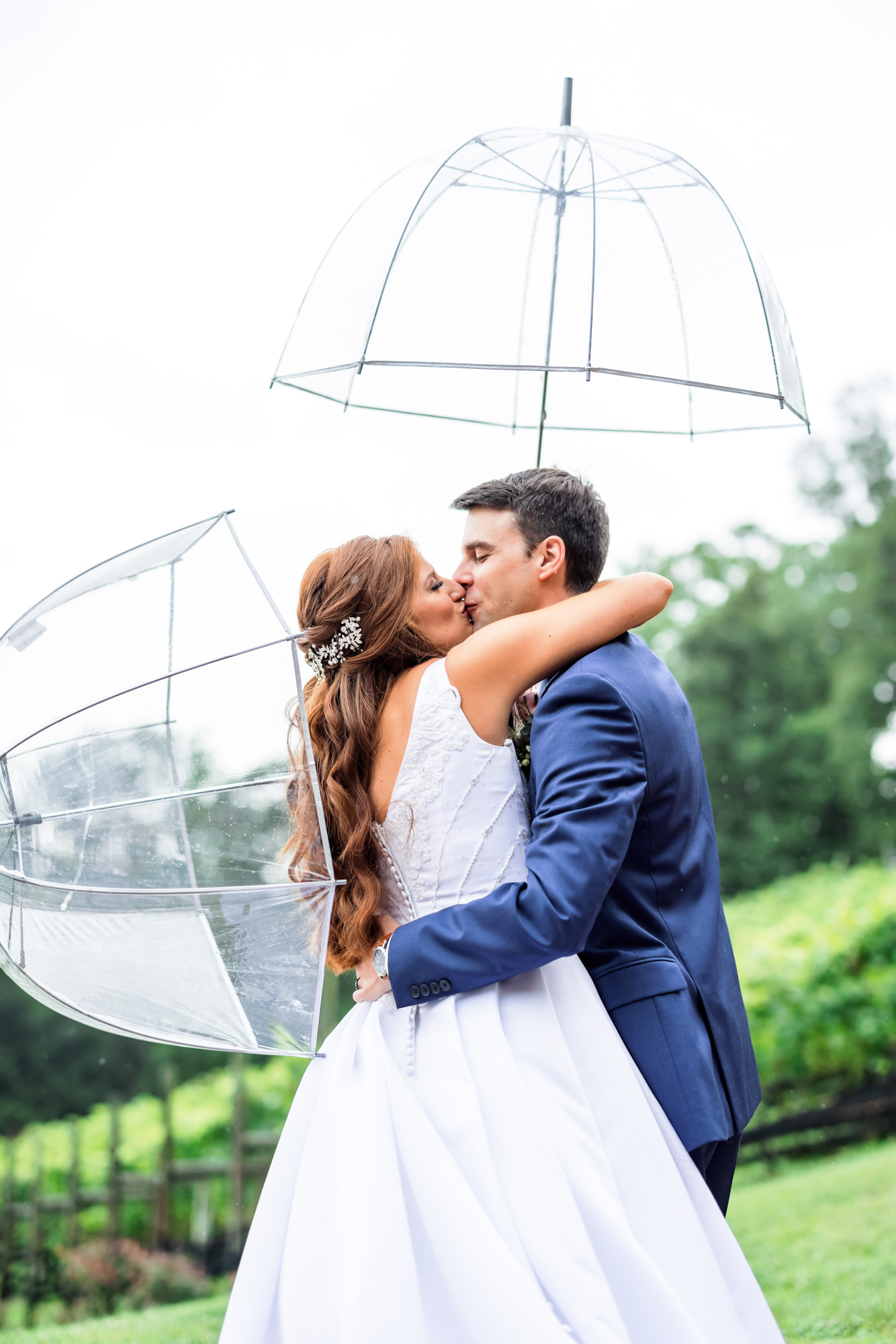wedding couple embracing while holding clear umbrellas during rainy first look