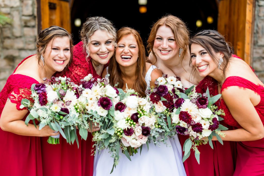 bride laughing with wedding party wearing red gowns during portraits