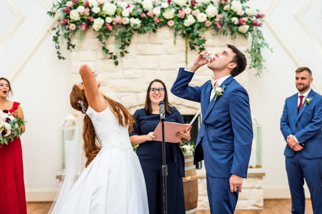 bride and groom drinking wine during wedding ceremony wearing classic white wedding dress and navy suit