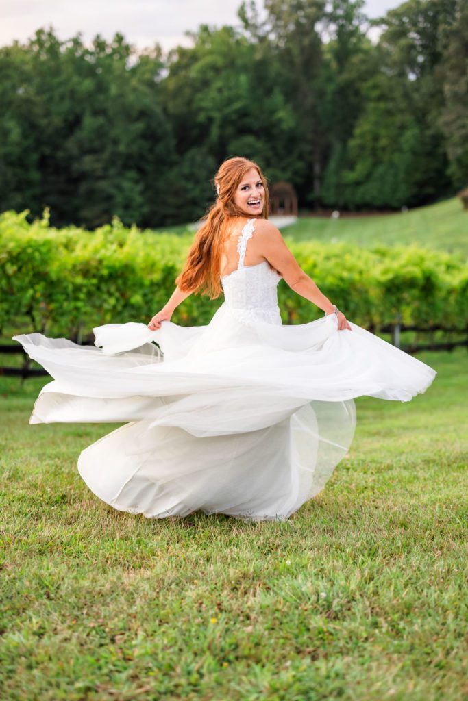 bride spinning dress around in green field with vineyards behind her
