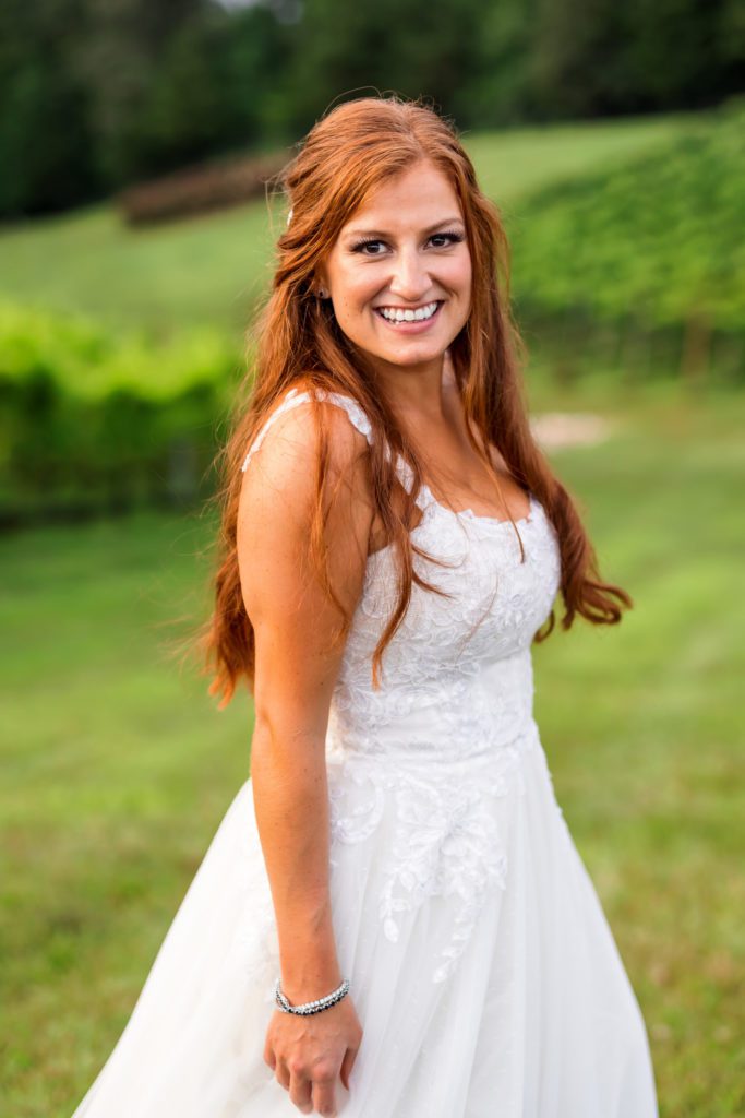 auburn haired bride looking into camera wearing simple wedding dress at winery