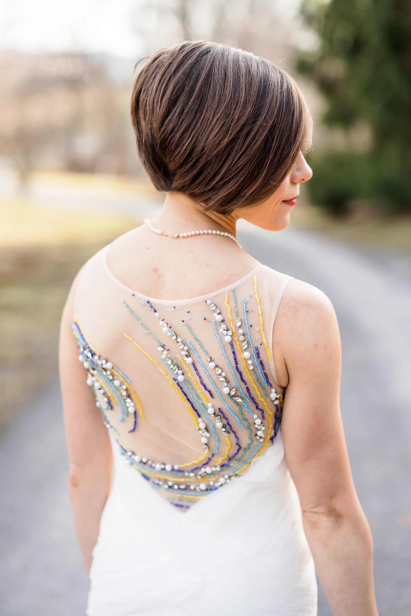 bride looking away from camera while back of dress is shown with intricate beading and pearls