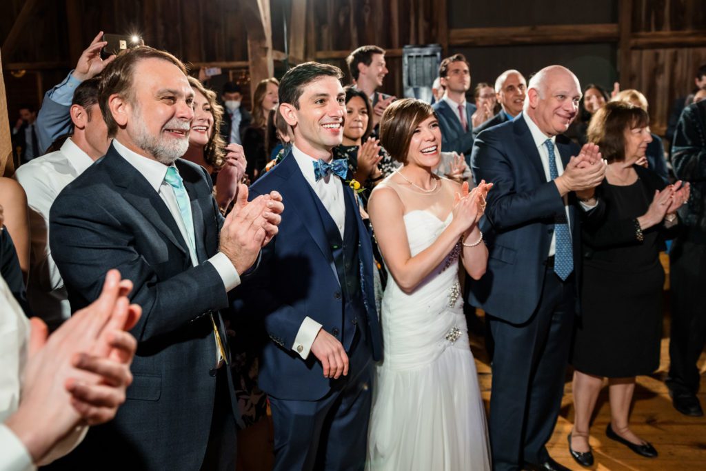 bride and groom clapping and laughing with guests during jewish wedding reception