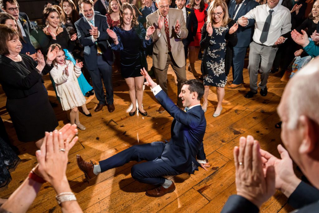groom break dancing during jewish wedding reception on wood floor