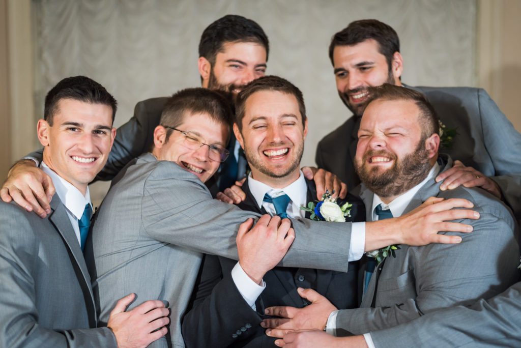 groom being hugged by groomsmen wearing gray suits