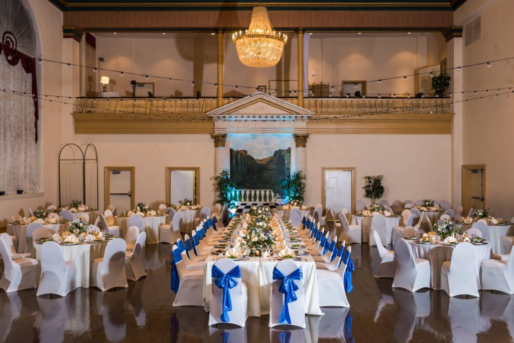 indoor wedding reception with long tables of white table cloths, blue bows