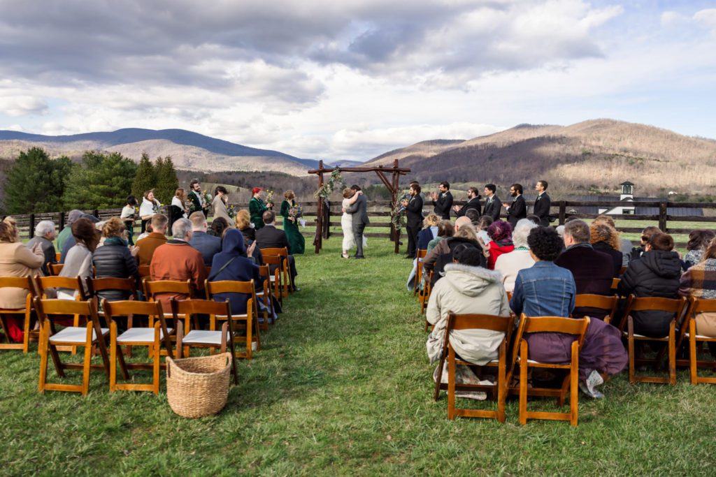 guests sitting in wooden chairs during outdoor ceremony