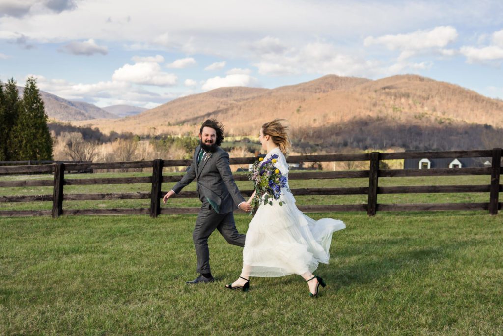 wedding couple running through field of grass after windy spring wedding ceremony