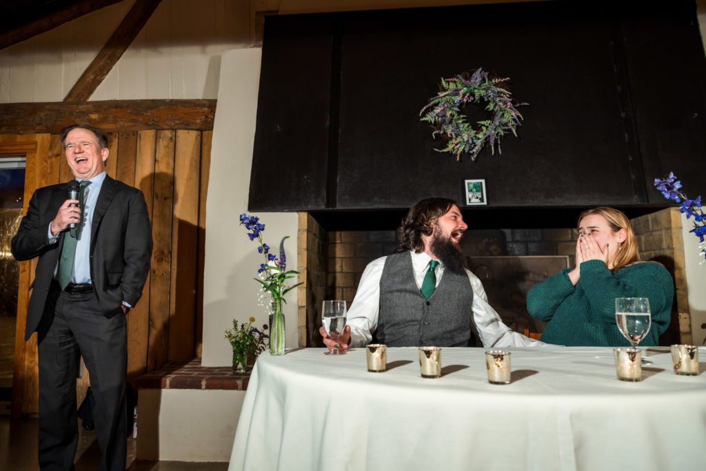 guests giving toasts while wedding couple sits at sweethearts table laughing