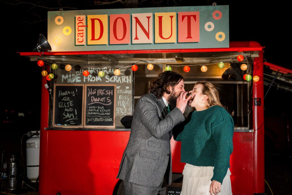 wedding couple kissing while eating carpe diem donuts to end their windy spring charlottesville wedding day