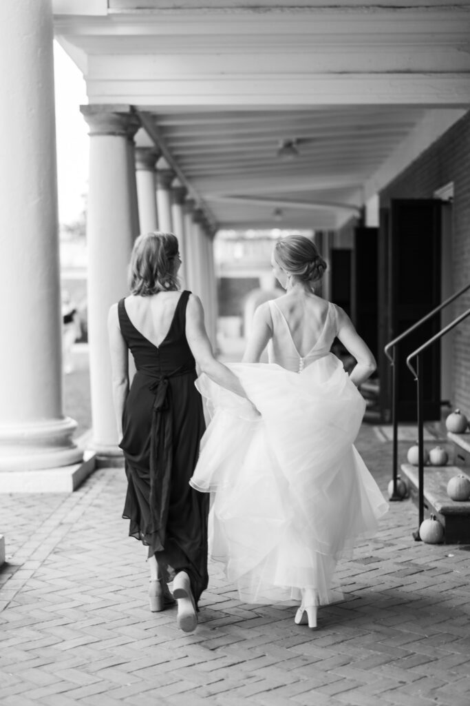 black and white portrait of bride walking with wedding party holding her gown