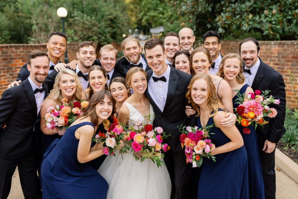 wedding party surrounding bride and groom wearing navy gowns and dark tuxedos