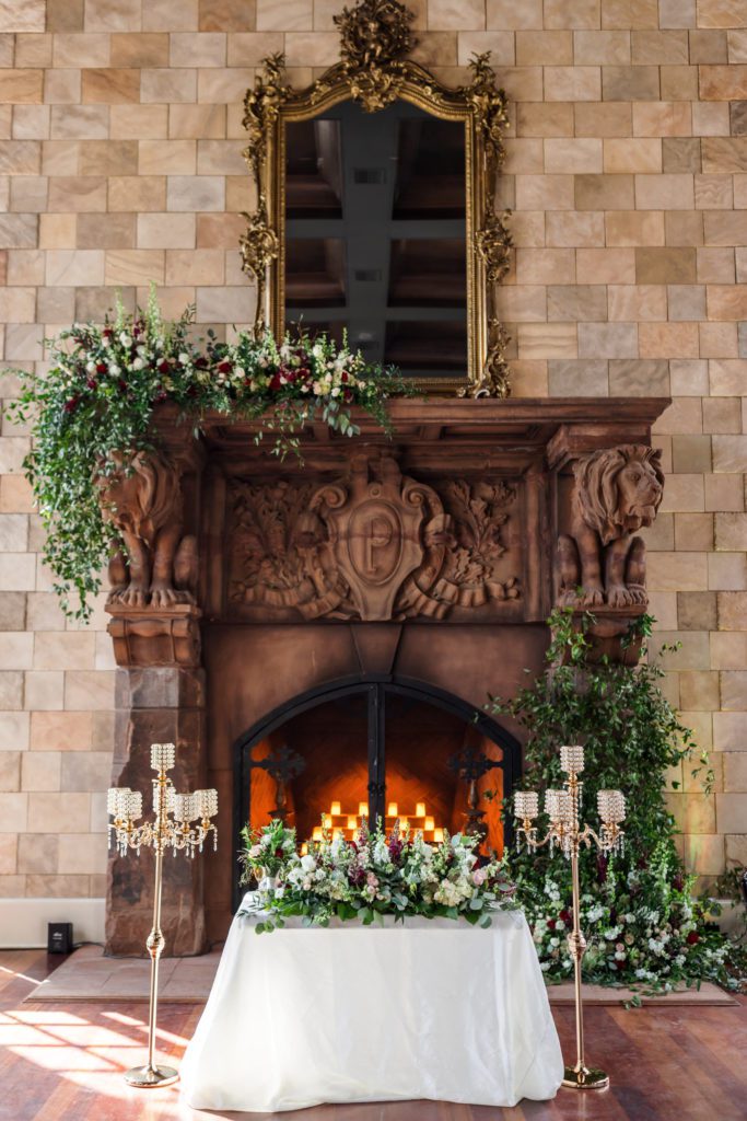 close up of sweethearts table and wood fireplace with greenery and florals