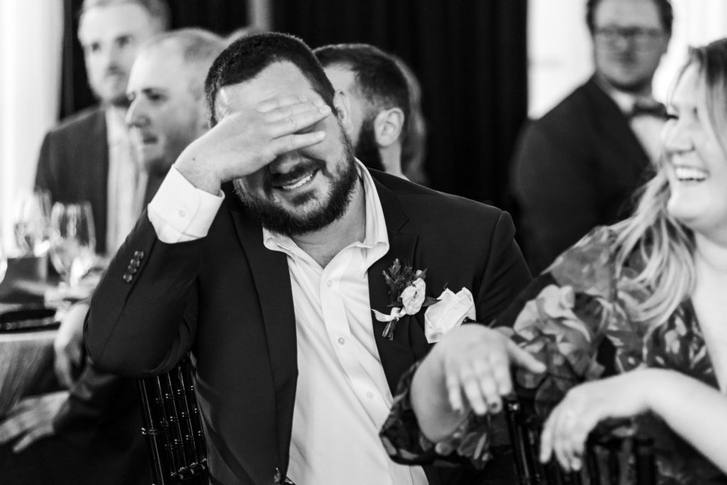 groomsmen smiling and covering eyes in embarrassment during toasts 