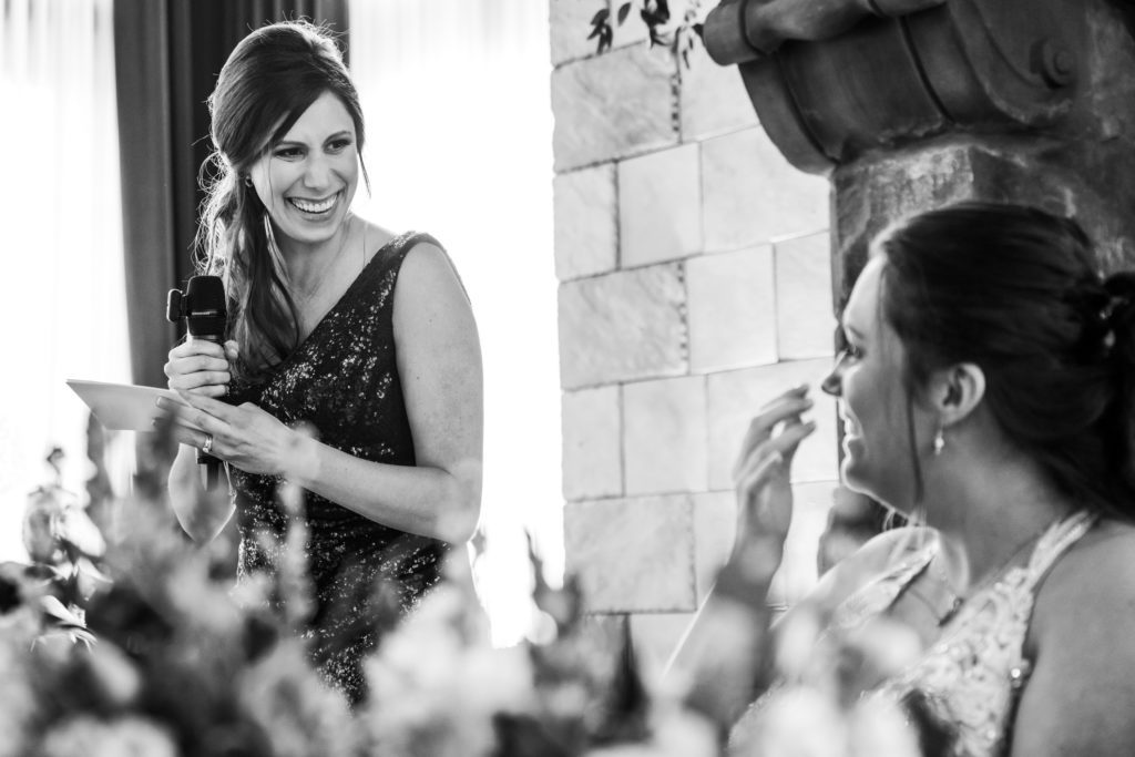 bride looking over at bridesmaid during toasts and speeches at wedding reception in black and white portrait