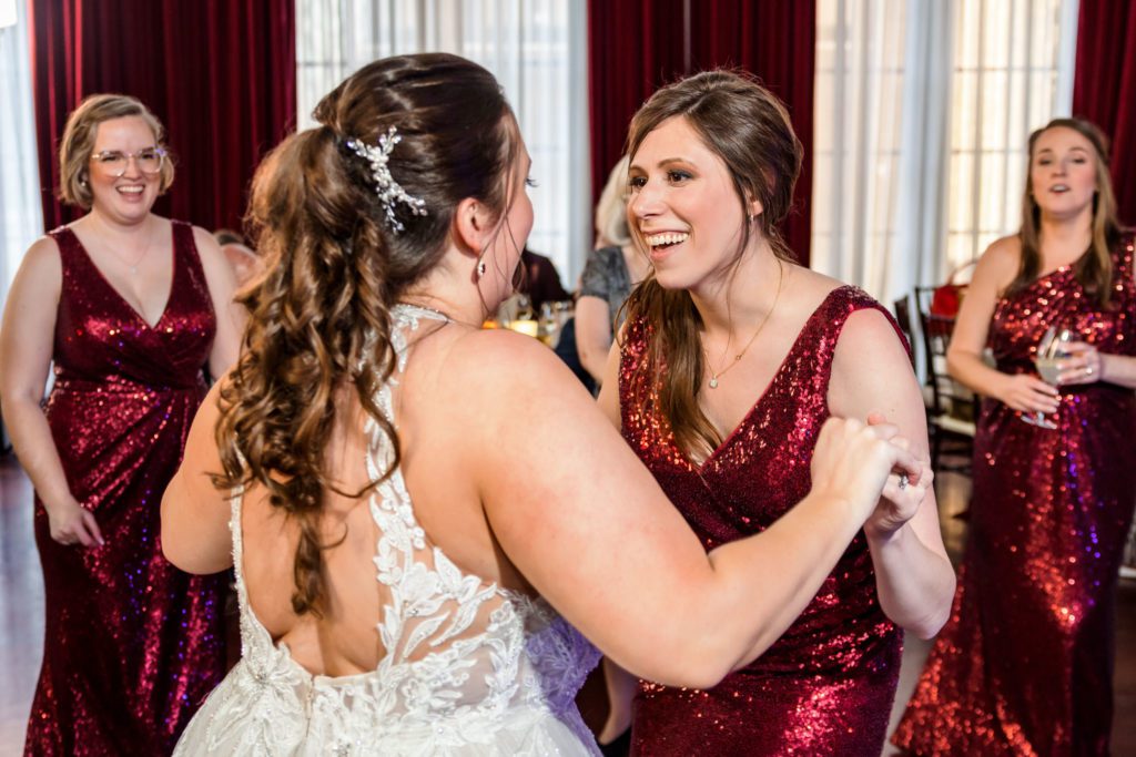 bride holding hands and celebrating with bridesmaid during reception