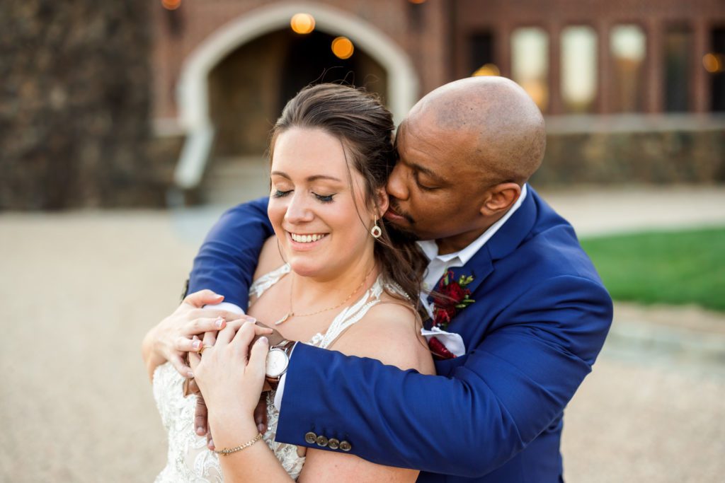 groom wrapping arms around bride's chest during sunset portraits