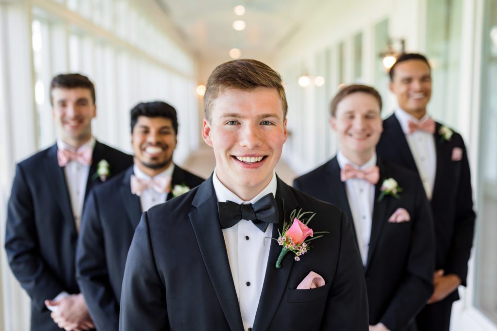groom standing with groomsmen behind him smiling during wedding party portraits
