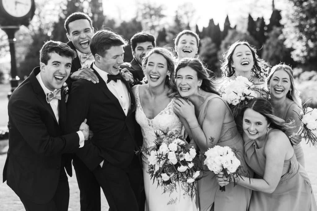 bridal couple laughing and celebrating with wedding party during portraits