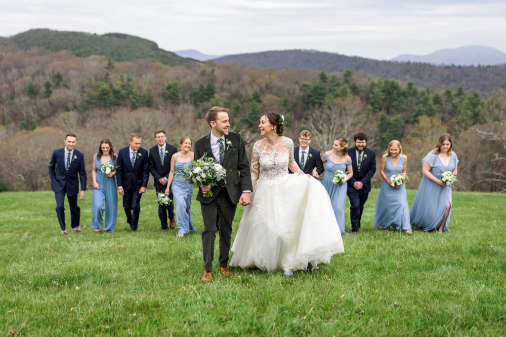 wedding couple walking in field with wedding party behind them