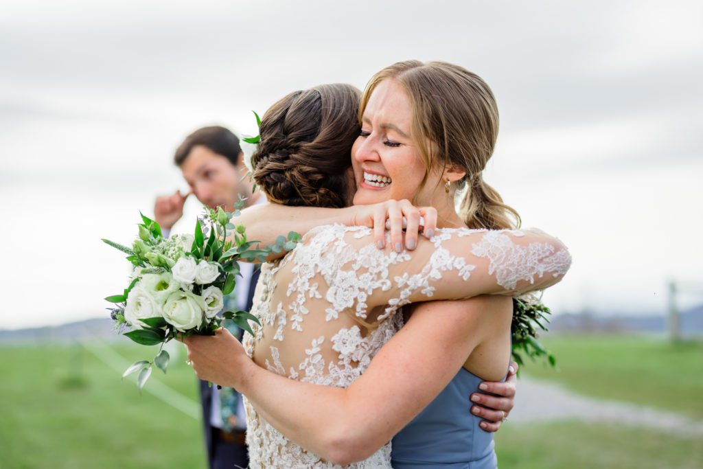 bride hugging bridesmaid wearing long sleeve lace wedding gown after ceremony