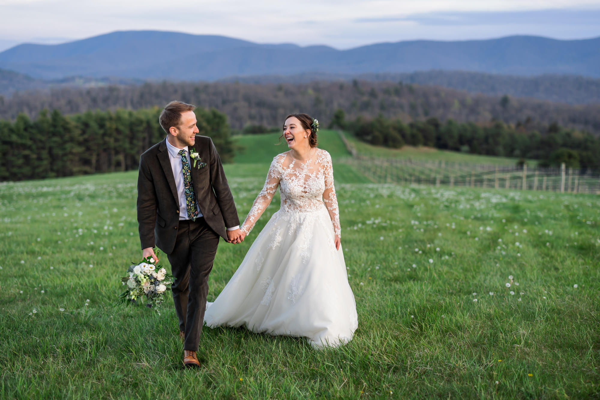 bride and groom holding hands and walking through grassy field during outdoor wedding portraits