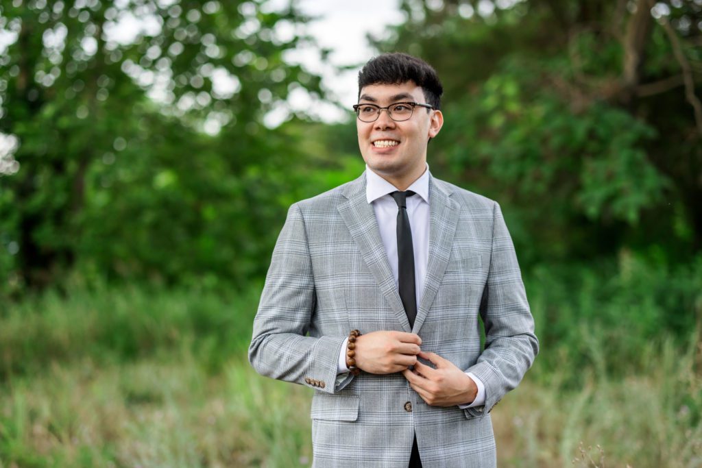 man wearing grey checkered blazer buttoning buttons at outdoor engagement session