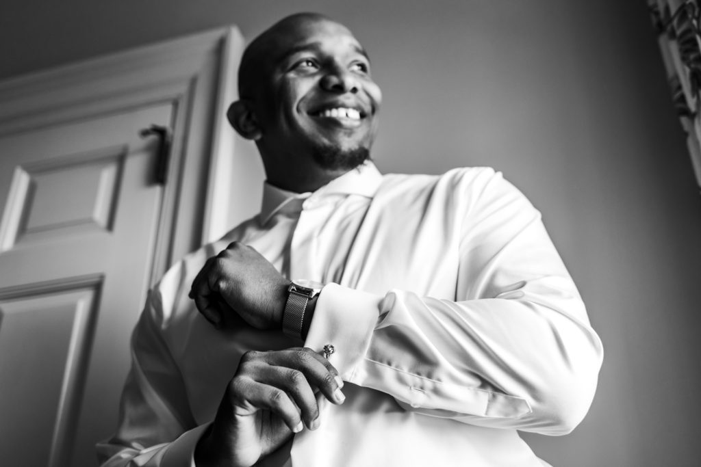 groom smiling and buttoning shirt while getting ready for spring black tie montalto wedding