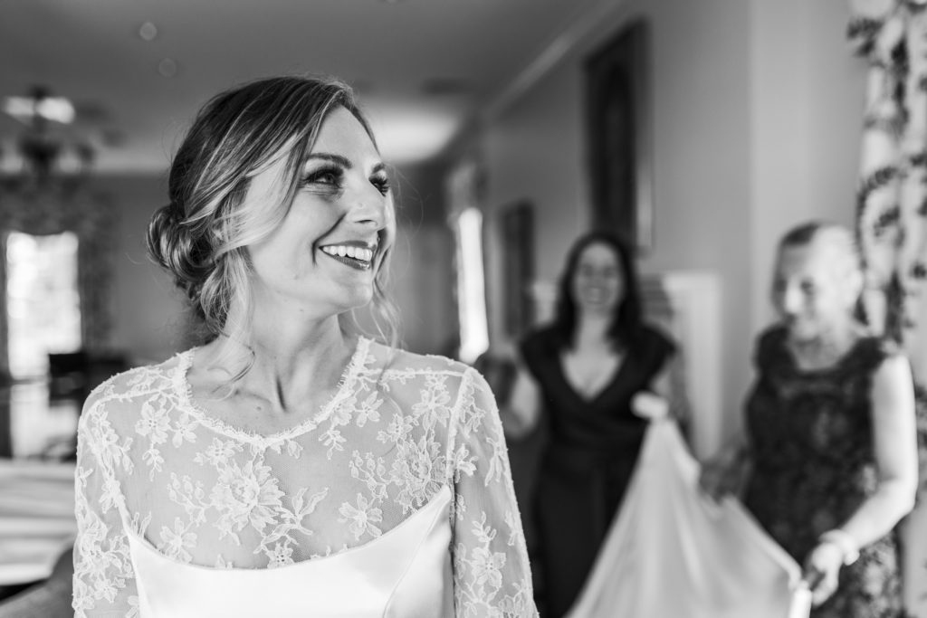 bride looking at bridal party smiling while bridal party fluffs gown