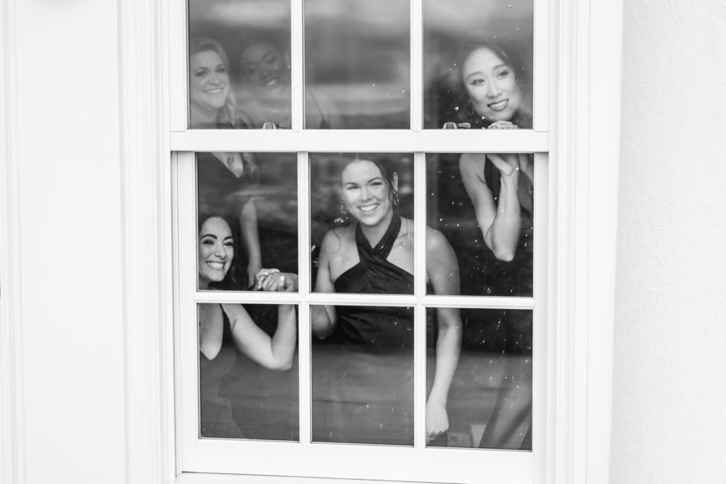 bridesmaids looking out of the window while bride and groom see one another for first time on wedding day