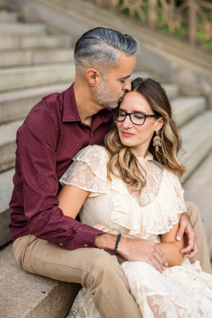 close up of man and woman sitting on steps, man's kissing woman's forehead