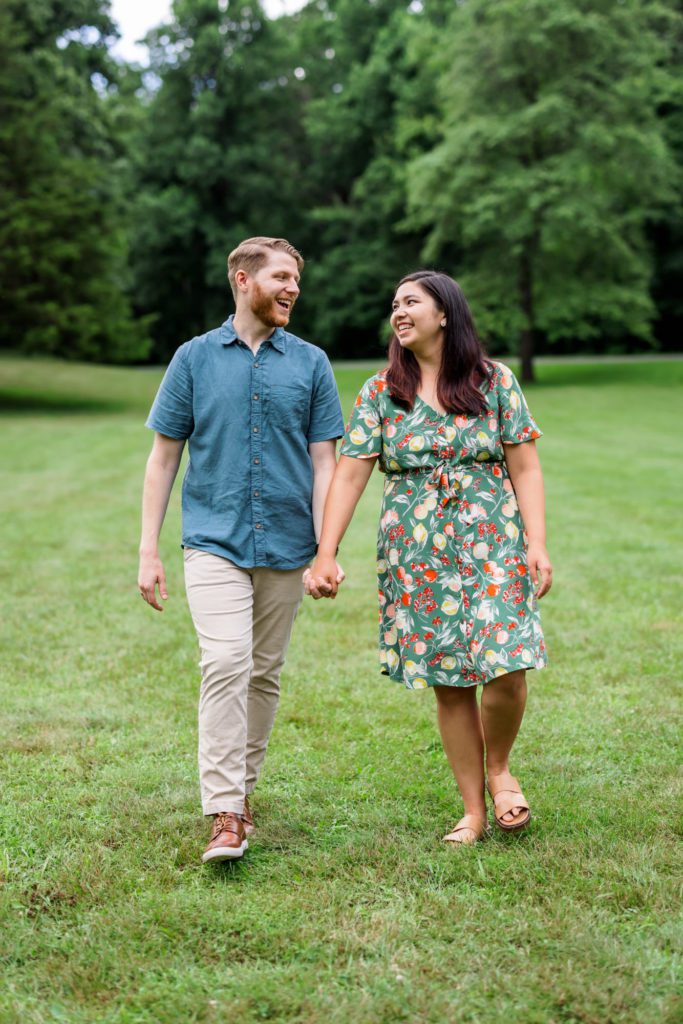 newly engaged couple walking hand in hand in field of grass