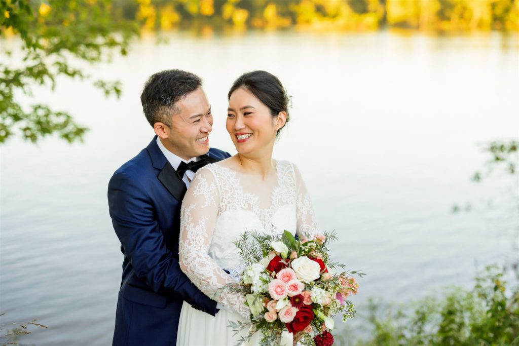 bridal couple embracing by waterside at Upper Shirley Vineyards