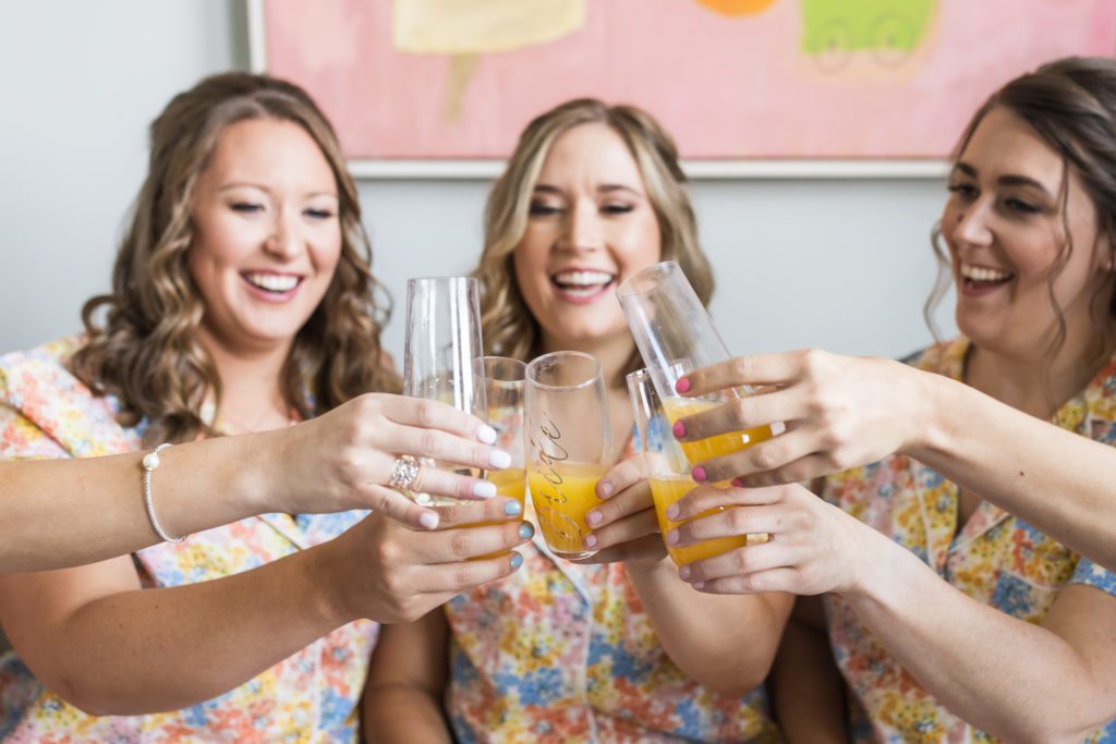 bride toasting mimosas with wedding party wearing matching floral pajamas before summer virginia house wedding