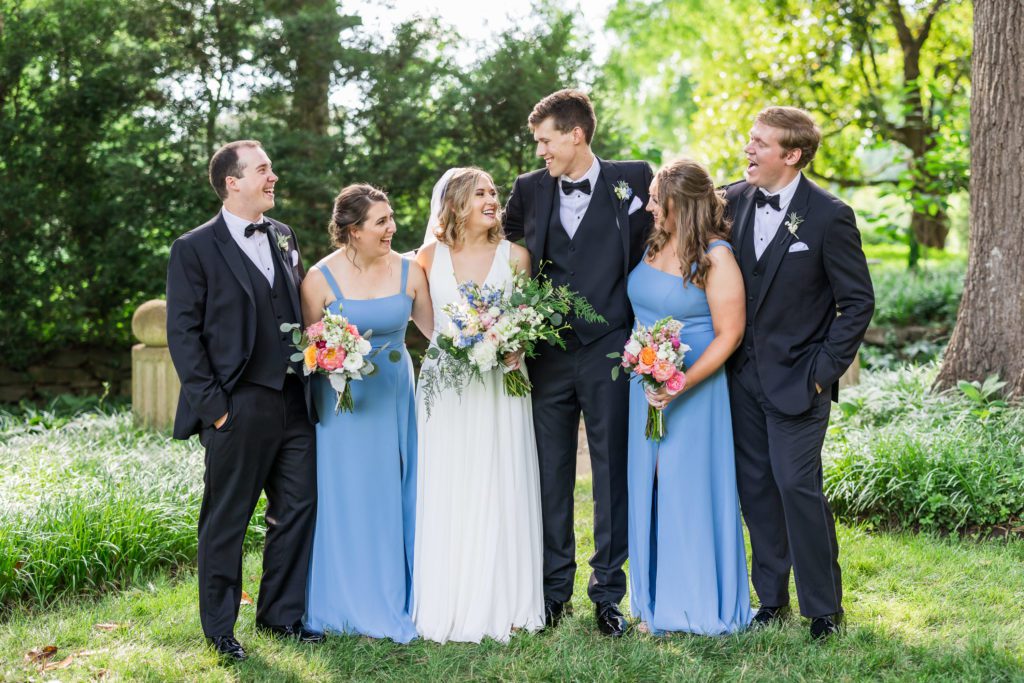 wedding couple standing with bridal party wearing blue dresses and holding bouquets ets 