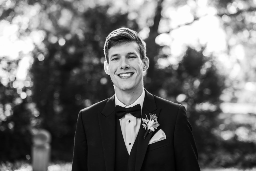 groom smiling wearing tuxedo in black and white portrait