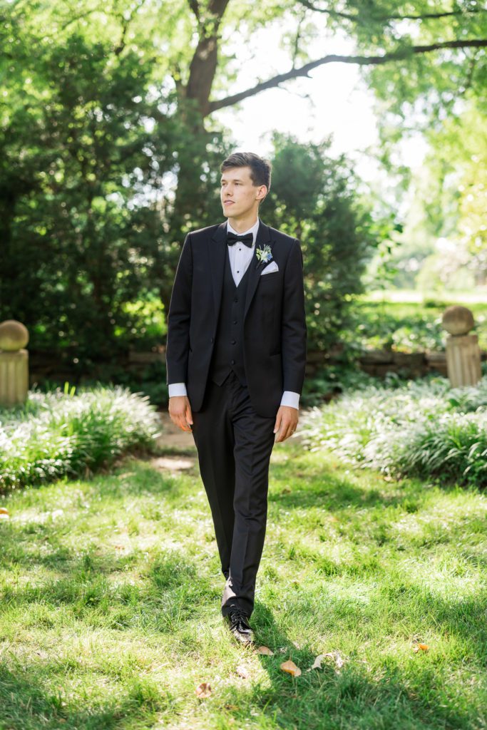 groom walking through grassy area wearing black tuxedo