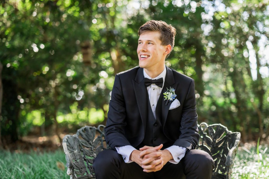 groom sitting on bench during outdoor portraits 