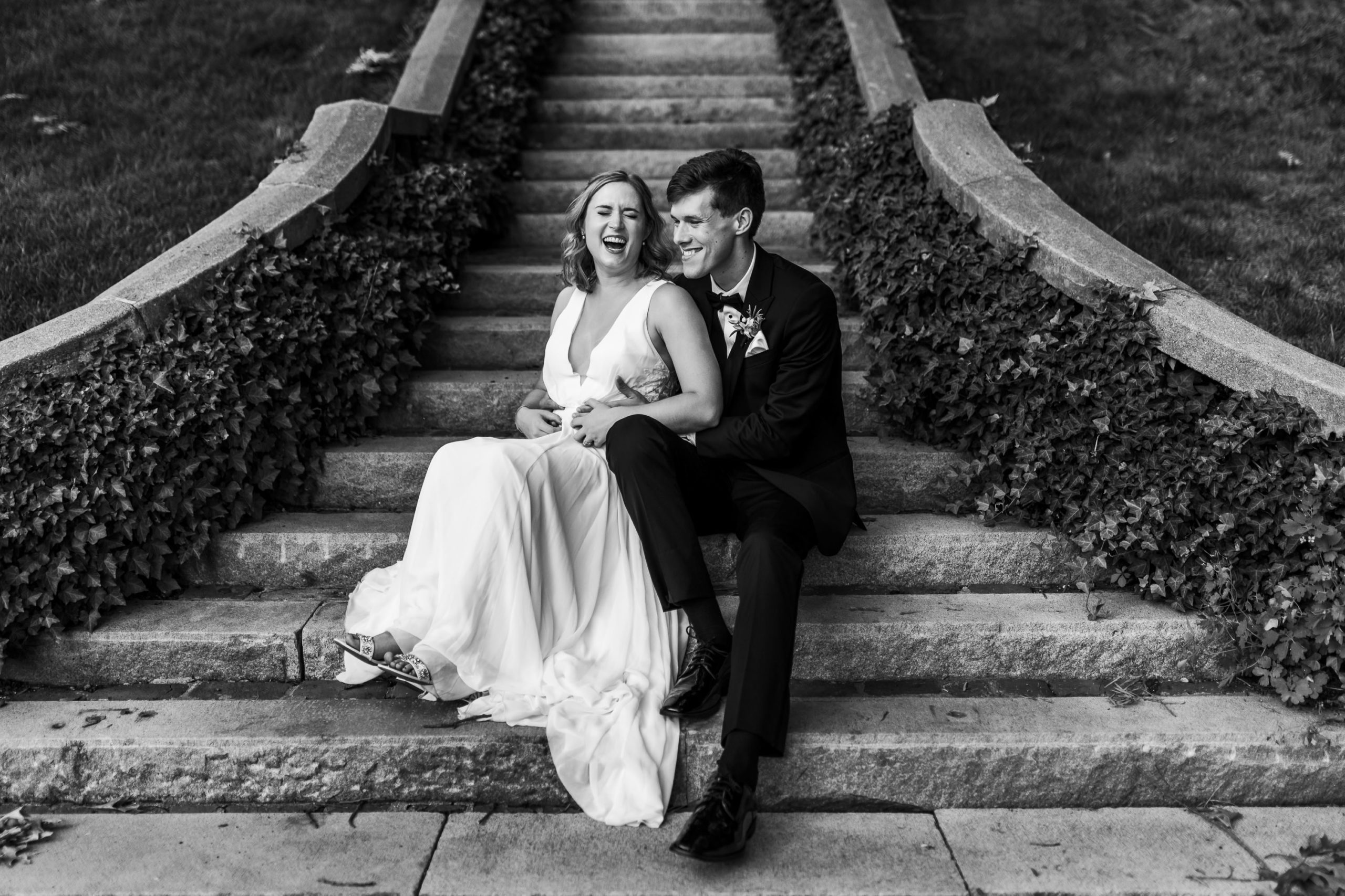 black and white portrait of bride and groom sitting on steps laughing together