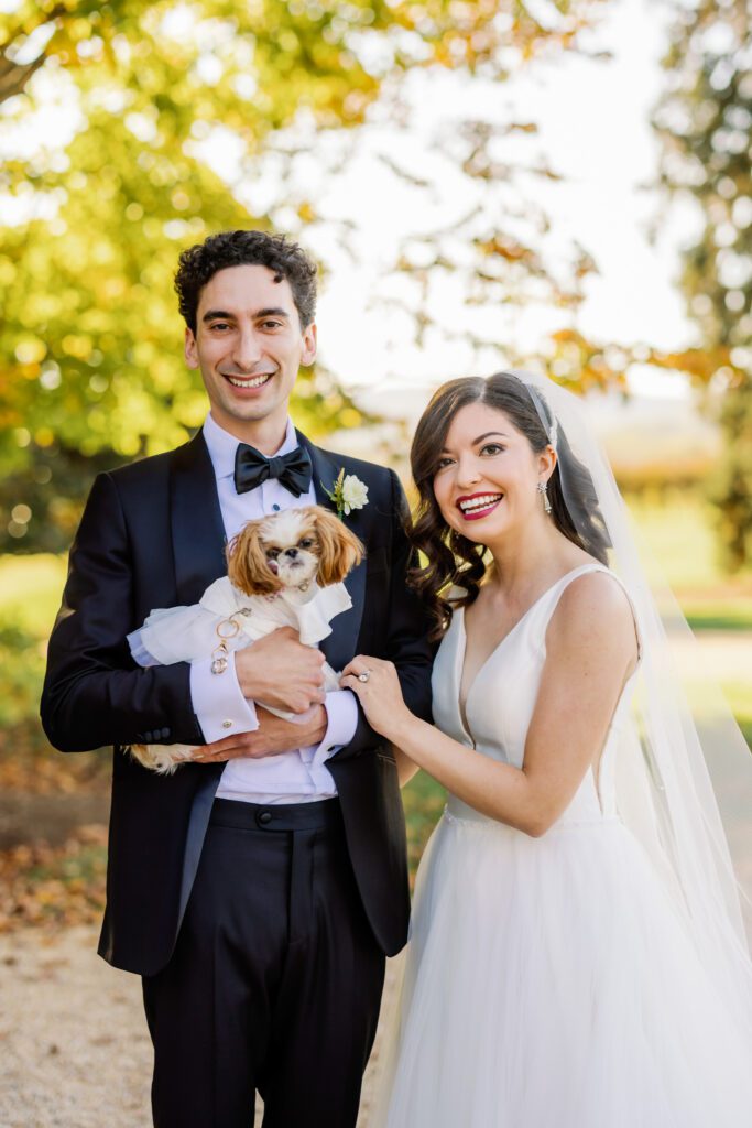 bride and groom smiling together while holding dog that's the ring bearer