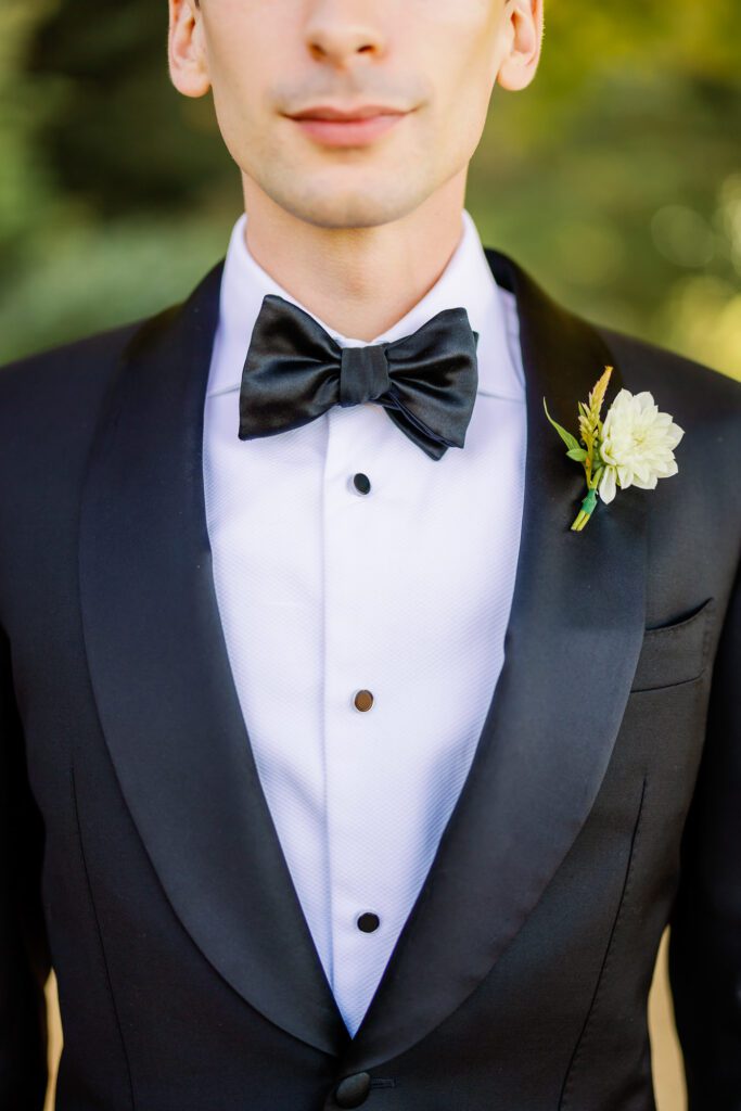 close up of tuxedo and black bowtie details with boutonniere on lapel