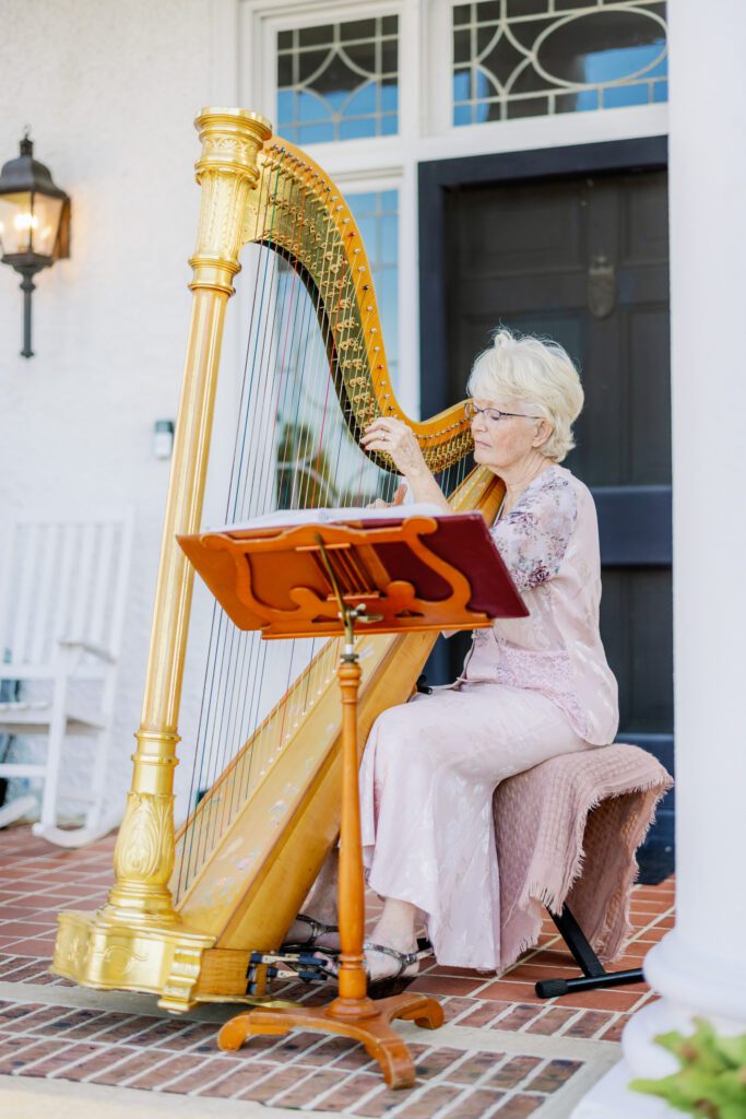 woman sitting down on stool playing the harp while bride and groom walk in