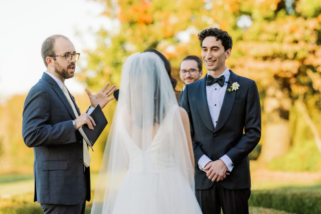 groom smiling as bride reads vows during wedding ceremony