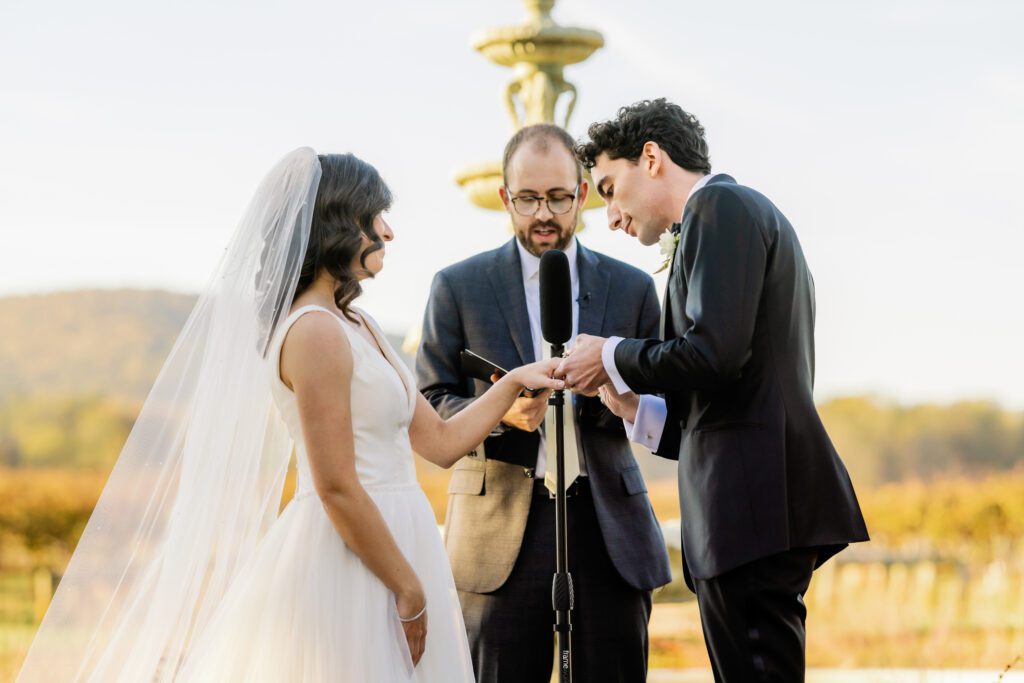 groom putting on wedding ring on bride's finger during wedding ceremony