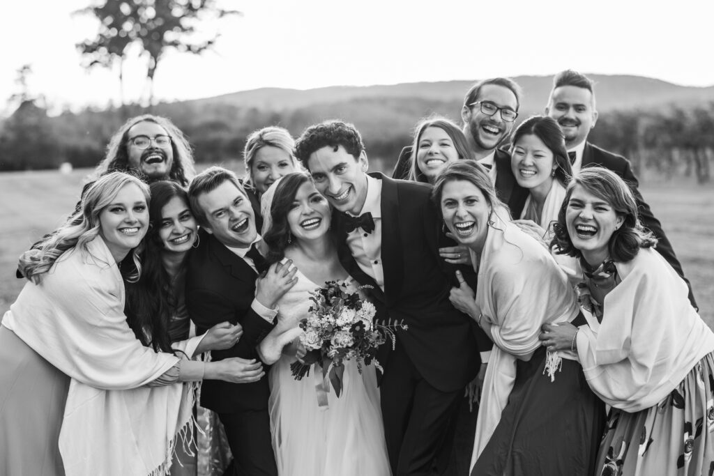 black and white photo of bride and groom smiling with wedding party smiling around them