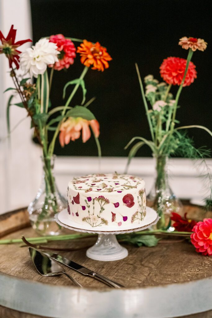 flowers in vases with wedding cake on stand with dried flowers on it
