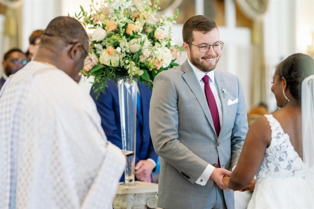 Groom smiling at bride during wedding ceremony while holding her hands