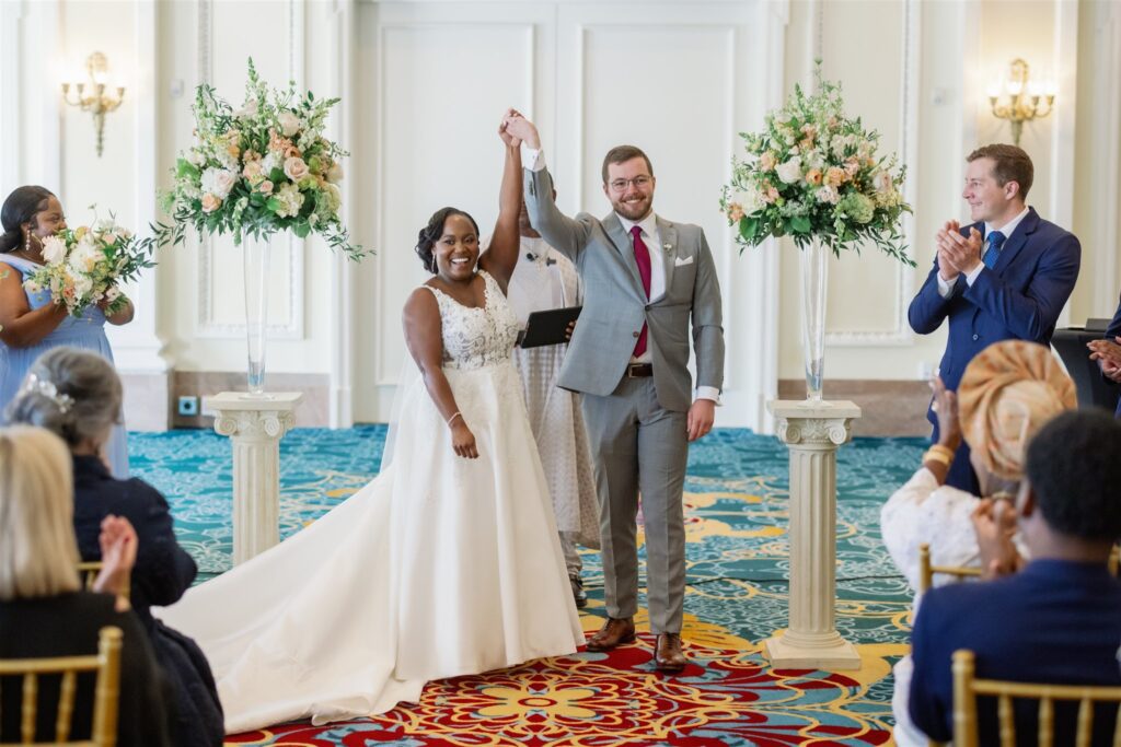 Bride and groom holding hands and lifting hands in the air to symbolize recent marriage