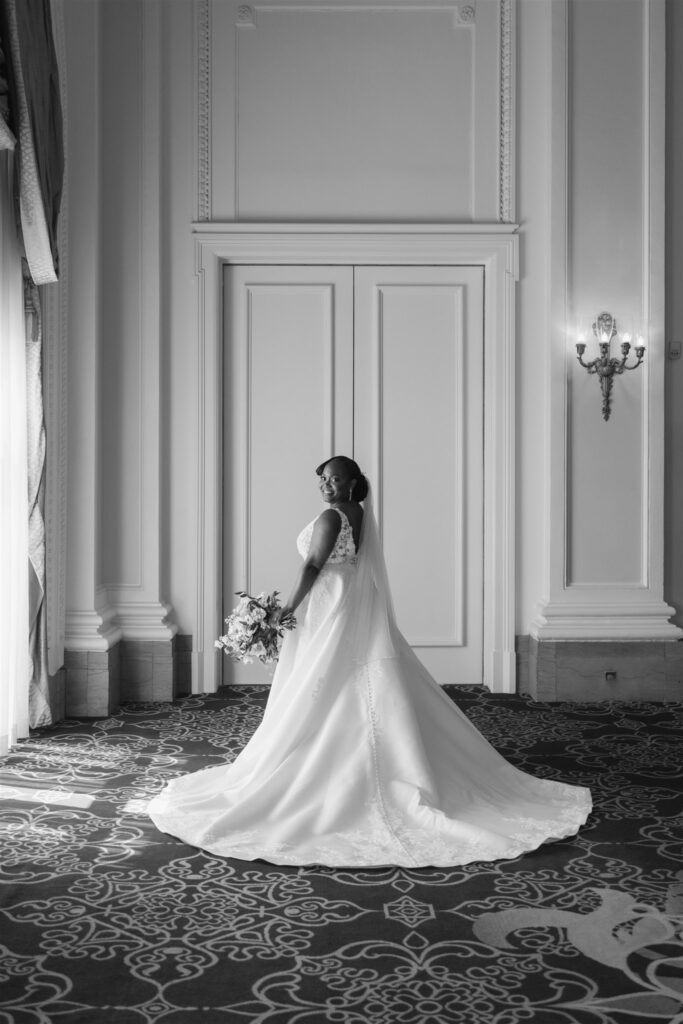 Black and white photo of bride in wedding gown holding bouquet and looking over shoulder