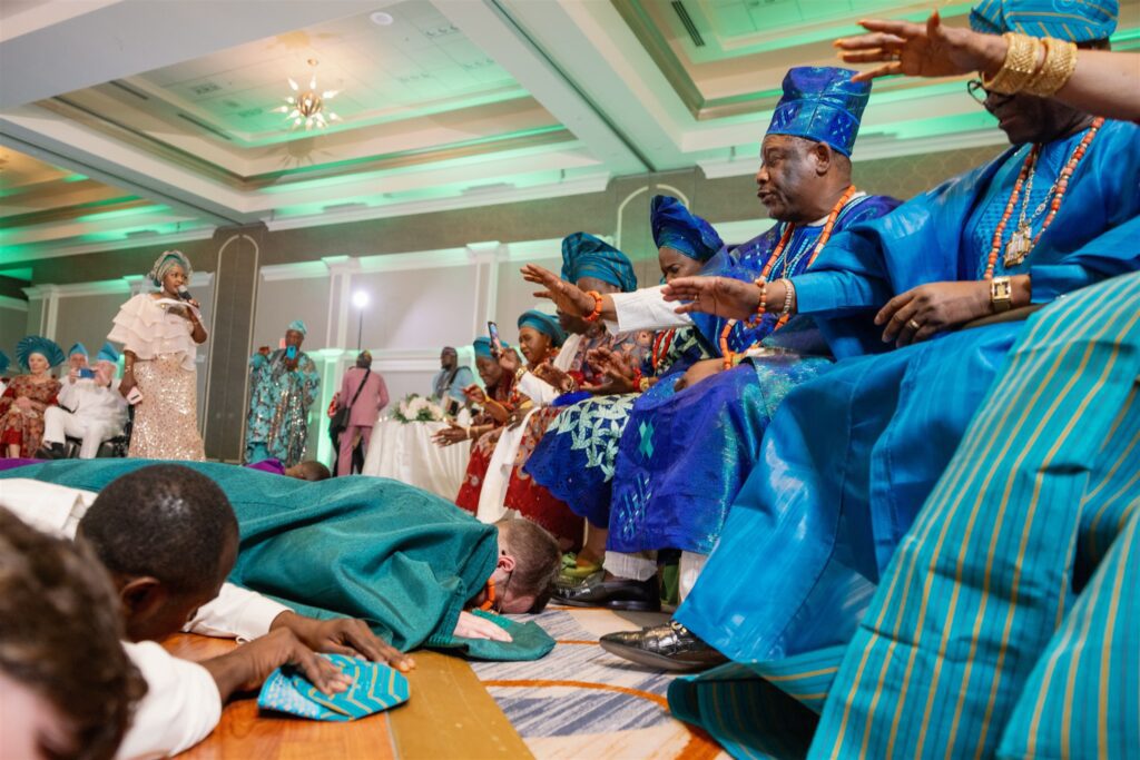 Groom bowing to parents feet while wearing traditional Nigerian clothing